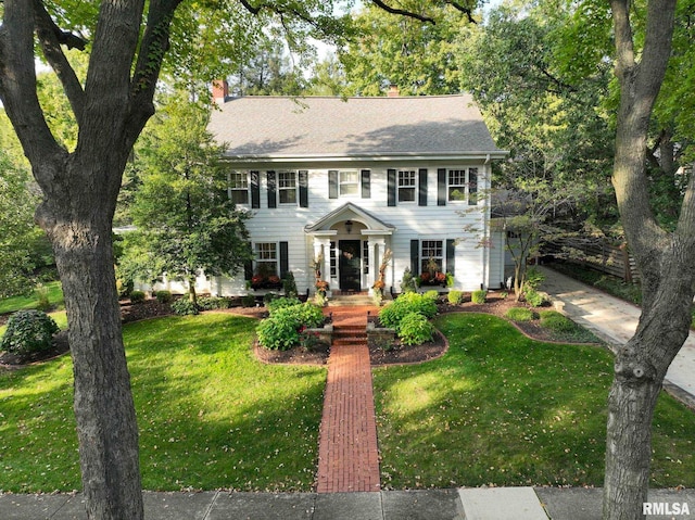 colonial home with a chimney, a front lawn, and roof with shingles