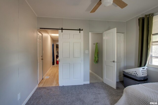 unfurnished bedroom featuring a barn door, ceiling fan, and light carpet