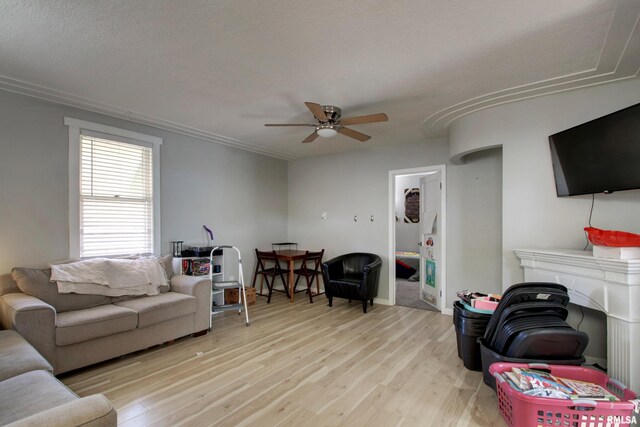 living room featuring ceiling fan, a fireplace, light hardwood / wood-style floors, and a textured ceiling