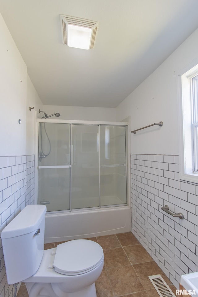 bathroom featuring tile walls, toilet, and combined bath / shower with glass door