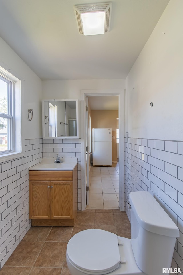 bathroom with tile patterned flooring, vanity, toilet, and tile walls