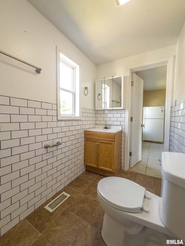 bathroom featuring tile patterned flooring, vanity, toilet, and tile walls