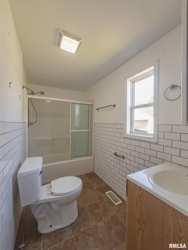 full bathroom with tile patterned flooring, toilet, combined bath / shower with glass door, tile walls, and vanity