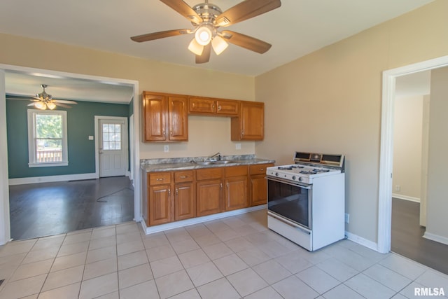 kitchen with light wood-type flooring, sink, white gas range oven, and ceiling fan