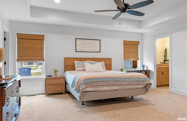 bedroom featuring a tray ceiling, light colored carpet, connected bathroom, and ceiling fan