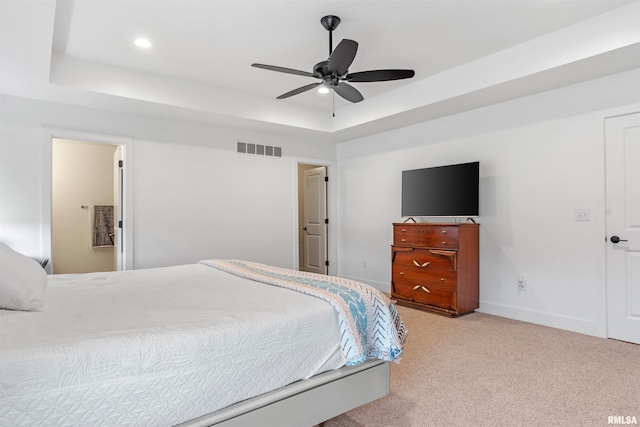 bedroom featuring ceiling fan, a raised ceiling, light carpet, and ensuite bathroom