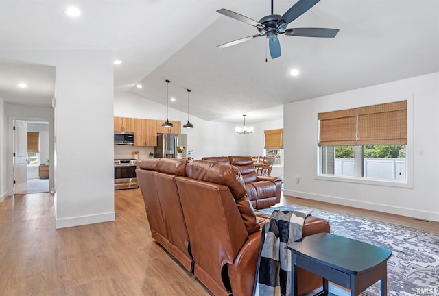 living room with ceiling fan with notable chandelier, lofted ceiling, and light hardwood / wood-style flooring