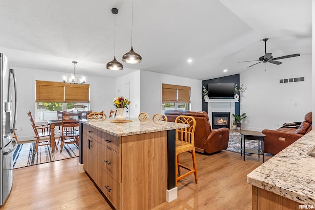 kitchen with ceiling fan with notable chandelier, light hardwood / wood-style flooring, hanging light fixtures, a center island, and light stone counters