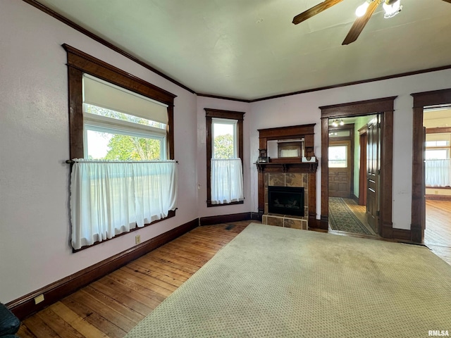 unfurnished living room featuring crown molding, hardwood / wood-style flooring, ceiling fan, and a tile fireplace