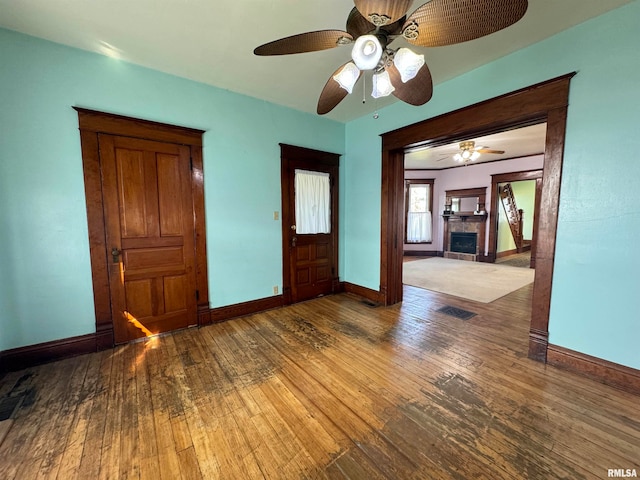 empty room featuring hardwood / wood-style floors, ceiling fan, and a tiled fireplace