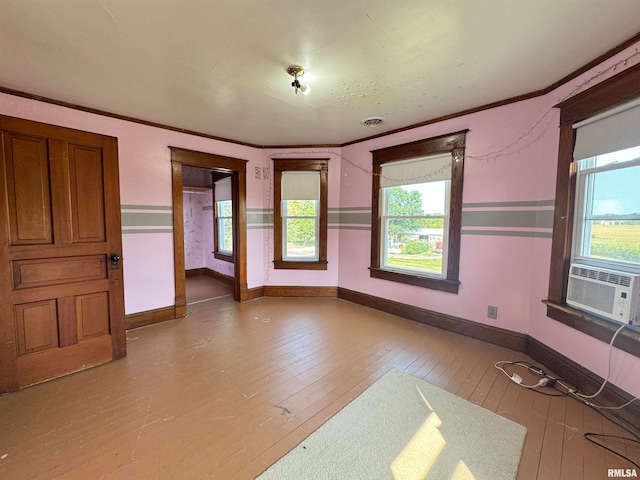 empty room with cooling unit, a healthy amount of sunlight, ornamental molding, and wood-type flooring