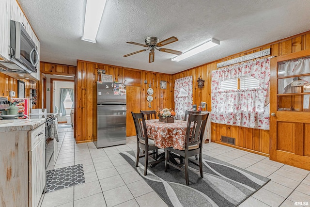 tiled dining space featuring ceiling fan, wooden walls, and a textured ceiling