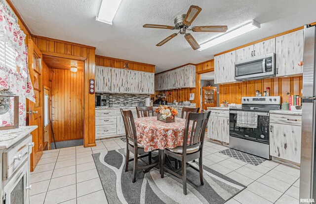 kitchen featuring a textured ceiling, light tile patterned floors, stainless steel appliances, ceiling fan, and wooden walls