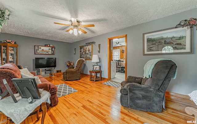 living room with ceiling fan, a textured ceiling, and light hardwood / wood-style flooring