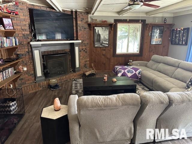 living area with wood finished floors, beamed ceiling, a fireplace, and ceiling fan