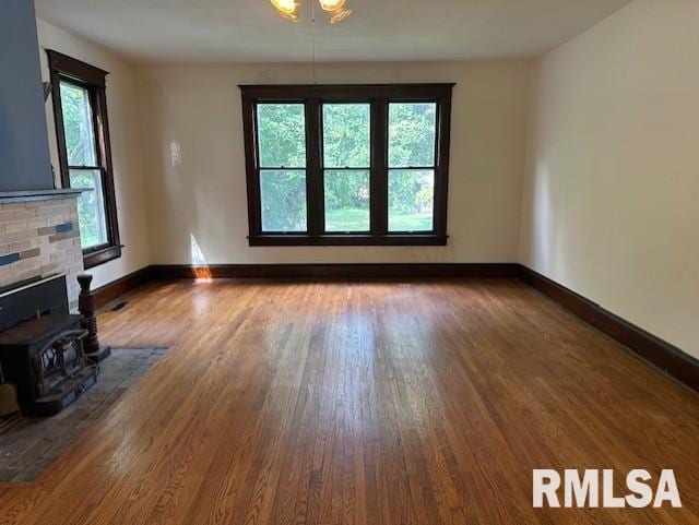 unfurnished living room featuring a healthy amount of sunlight, wood-type flooring, and a wood stove