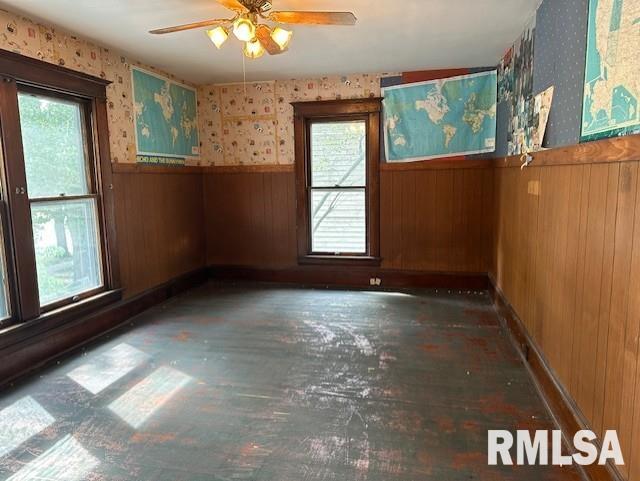 empty room featuring a wealth of natural light, ceiling fan, and wooden walls