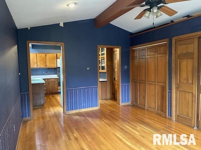 unfurnished bedroom featuring ceiling fan, a closet, light wood-type flooring, and lofted ceiling with beams