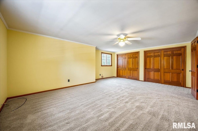 unfurnished bedroom with ceiling fan, carpet, crown molding, and multiple closets