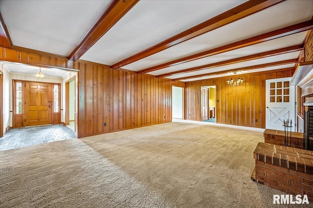 unfurnished living room with a notable chandelier, wooden walls, ornamental molding, carpet, and beam ceiling