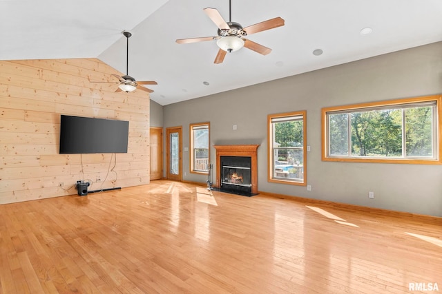 unfurnished living room featuring ceiling fan, lofted ceiling, wood walls, and light hardwood / wood-style flooring