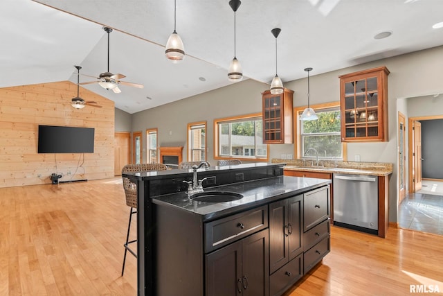 kitchen featuring an island with sink, wood walls, light wood-type flooring, ceiling fan, and stainless steel dishwasher