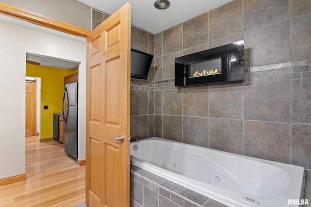 bathroom with a textured ceiling, tiled tub, and hardwood / wood-style floors