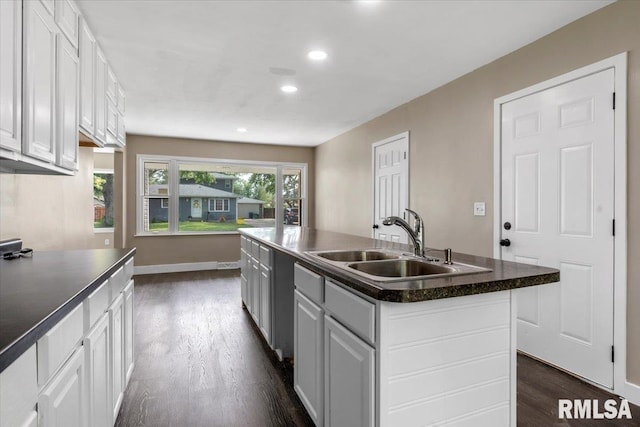 kitchen with a kitchen island with sink, sink, dark hardwood / wood-style flooring, and white cabinetry