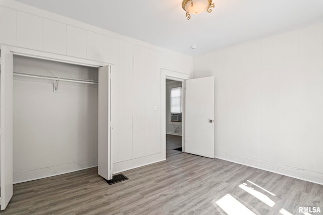 unfurnished bedroom with wood-type flooring, a closet, and cooling unit