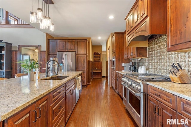 kitchen with wood-type flooring, sink, hanging light fixtures, premium appliances, and light stone countertops