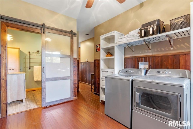 clothes washing area with ceiling fan, hardwood / wood-style flooring, a barn door, and washer and dryer