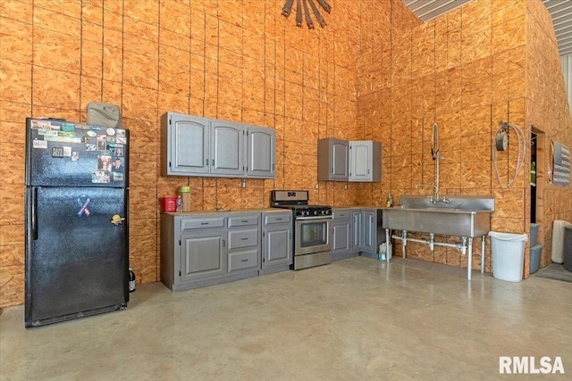 interior space featuring gray cabinetry, stainless steel range, black fridge, and concrete floors