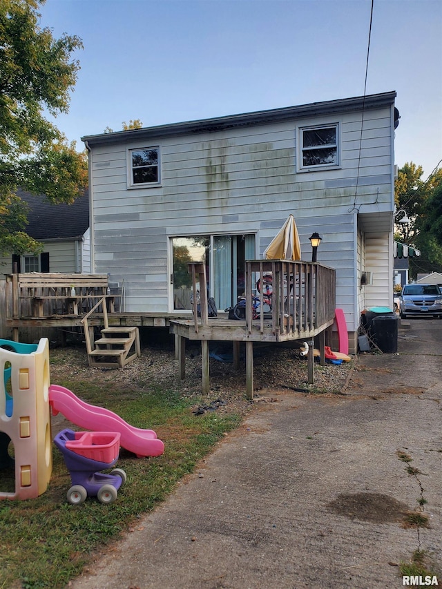 rear view of property featuring a playground and a wooden deck