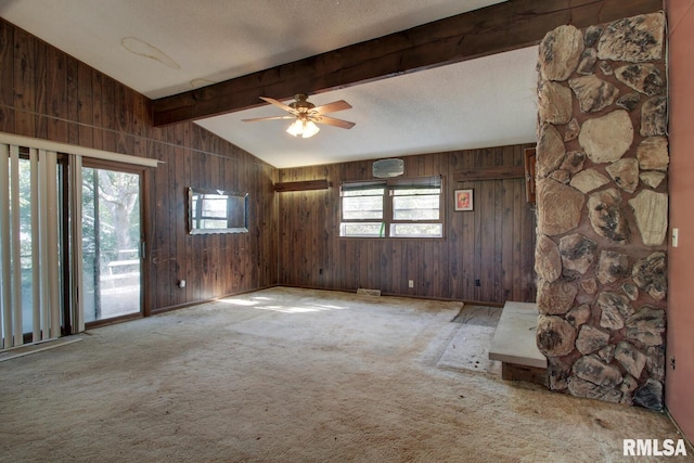 unfurnished living room featuring wooden walls, plenty of natural light, and lofted ceiling with beams