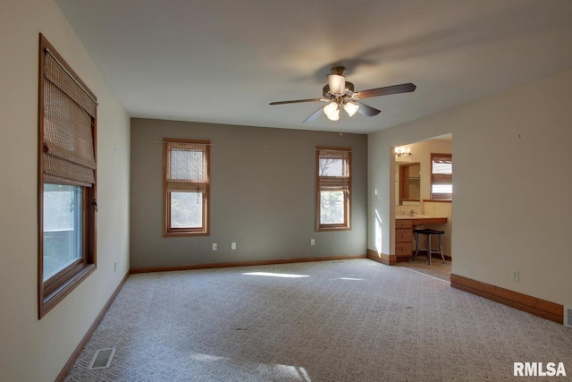 unfurnished living room featuring built in desk, light carpet, and ceiling fan