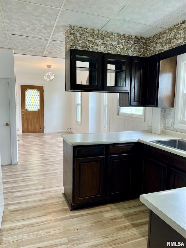 kitchen with light wood-type flooring, kitchen peninsula, dark brown cabinets, and tasteful backsplash