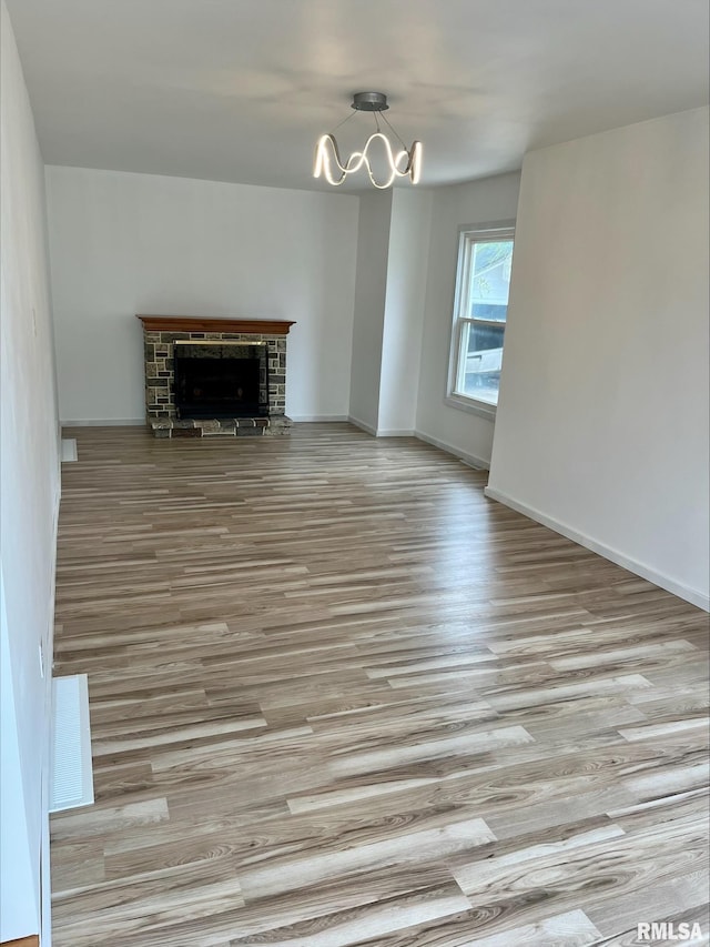 unfurnished living room featuring baseboards, a chandelier, wood finished floors, and a fireplace