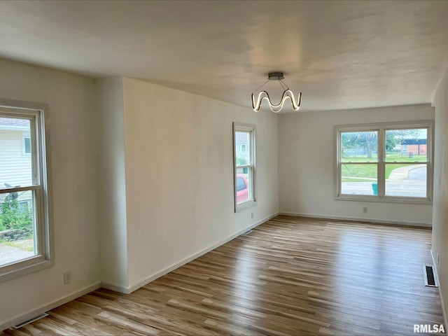 spare room featuring visible vents, wood finished floors, a notable chandelier, and baseboards