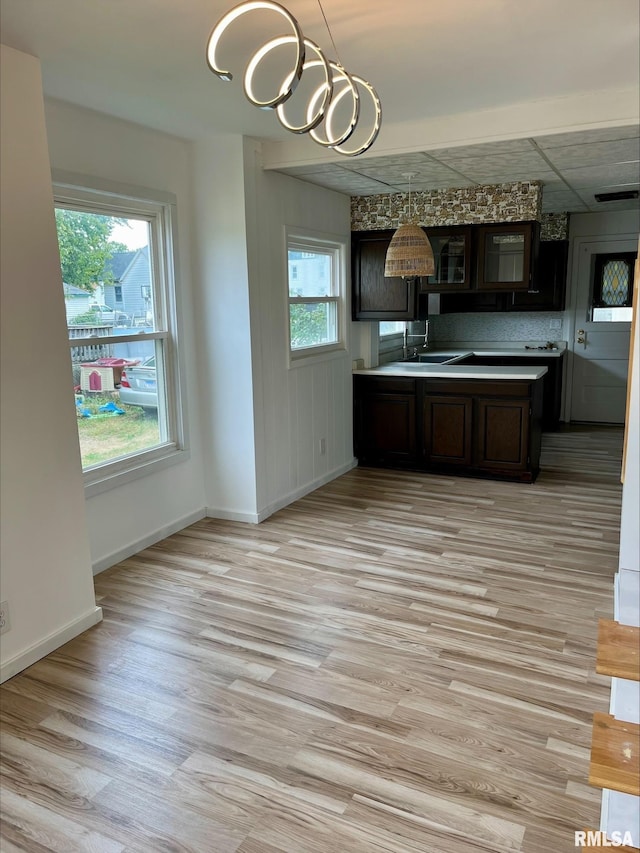 kitchen featuring an inviting chandelier, a sink, light wood-style flooring, baseboards, and dark brown cabinets