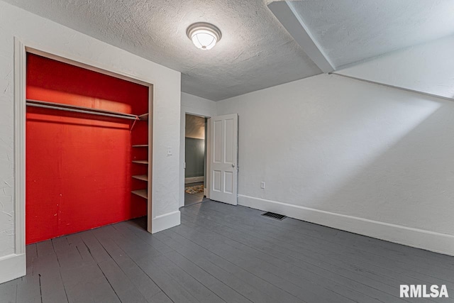 unfurnished bedroom with a textured ceiling, dark wood-type flooring, and a closet