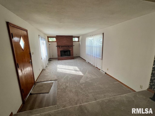 unfurnished living room with light colored carpet, a textured ceiling, a wealth of natural light, and a brick fireplace