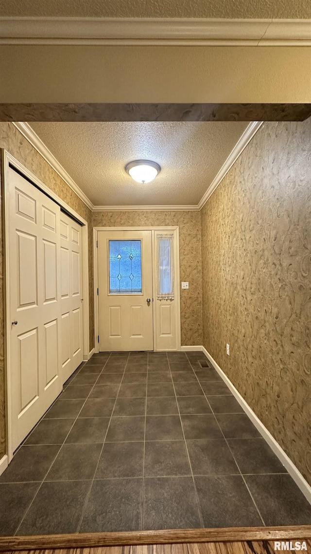 doorway featuring dark tile patterned flooring, a textured ceiling, and ornamental molding