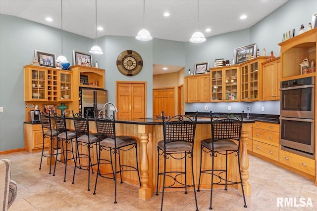 kitchen with appliances with stainless steel finishes, a kitchen breakfast bar, a towering ceiling, decorative light fixtures, and a kitchen island with sink