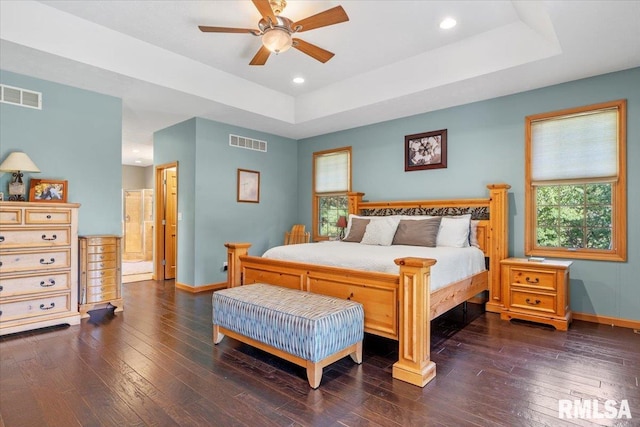 bedroom featuring ceiling fan, a tray ceiling, connected bathroom, and dark hardwood / wood-style flooring