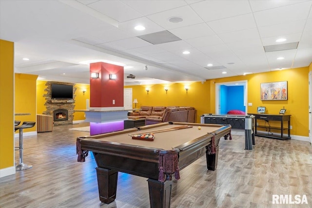 playroom featuring a stone fireplace, billiards, a drop ceiling, and light hardwood / wood-style flooring