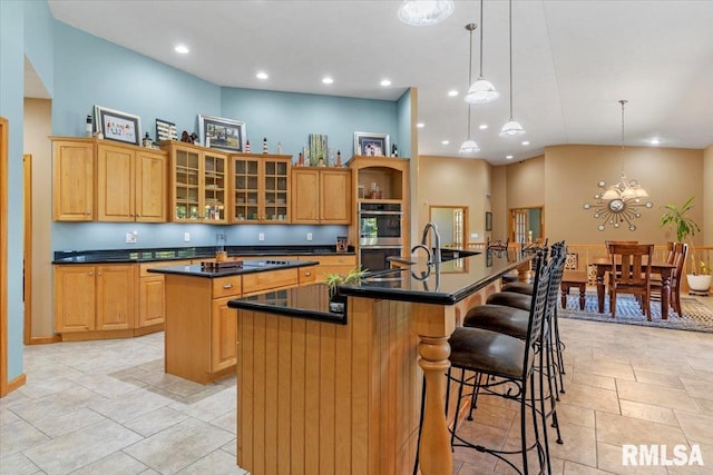 kitchen with a chandelier, an island with sink, a kitchen bar, a towering ceiling, and decorative light fixtures