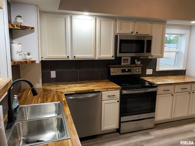 kitchen with sink, stainless steel appliances, wood counters, tasteful backsplash, and white cabinets