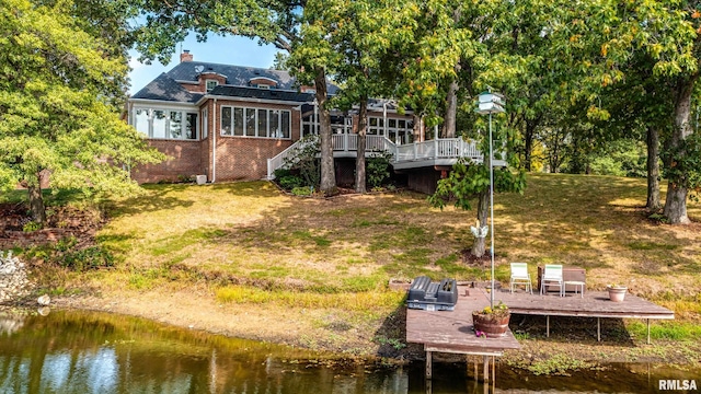 back of property with a lawn and a deck with water view