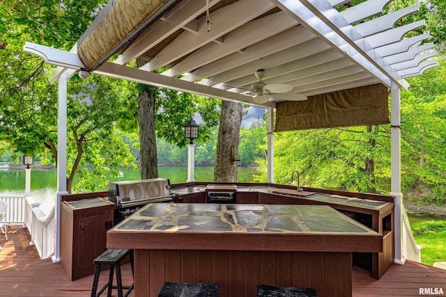 wooden terrace featuring a wet bar, a pergola, a water view, ceiling fan, and grilling area