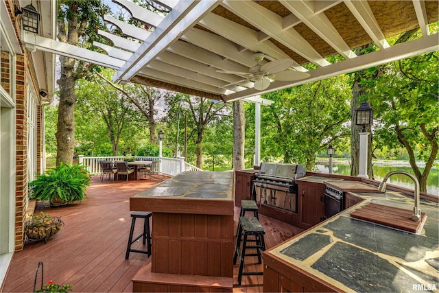 deck featuring exterior kitchen, a water view, ceiling fan, and a grill